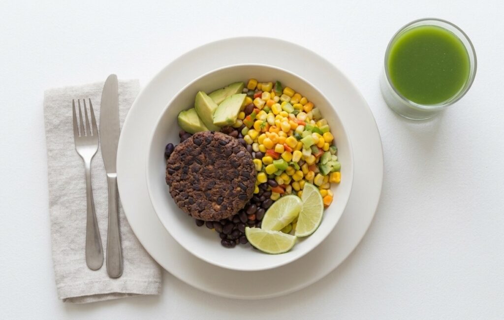 Veggie burger with a side of mixed vegetables and chunks of avocado with a green smoothie for a drink