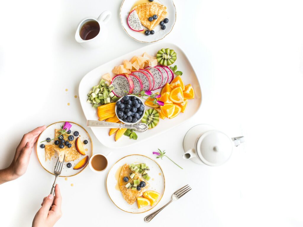 Plates of sliced fruit like oranges and kiwis with side of pancakes