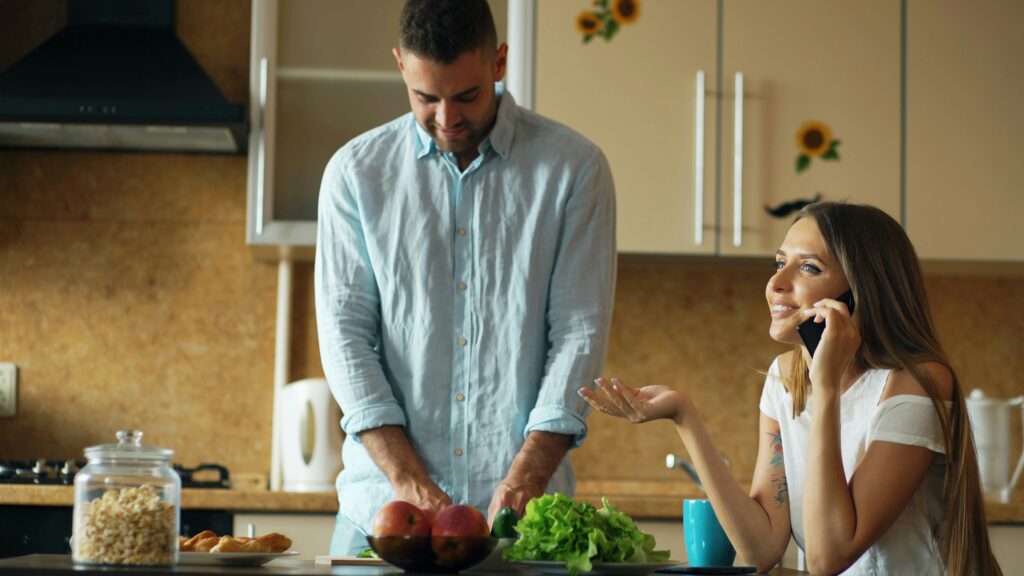 Man chopping vegetables with a woman near him talking on the phone